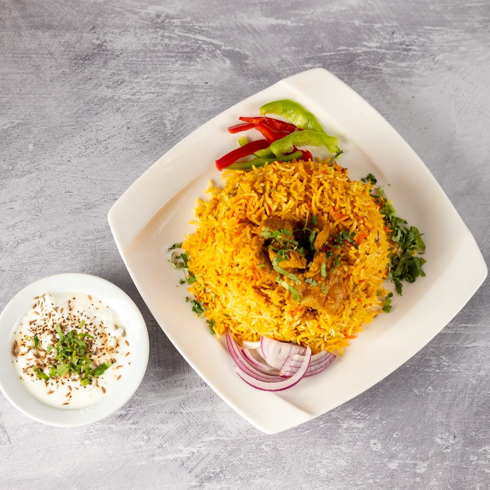 Chicken biryani with red and green peppers, red onions, and a side of raita.