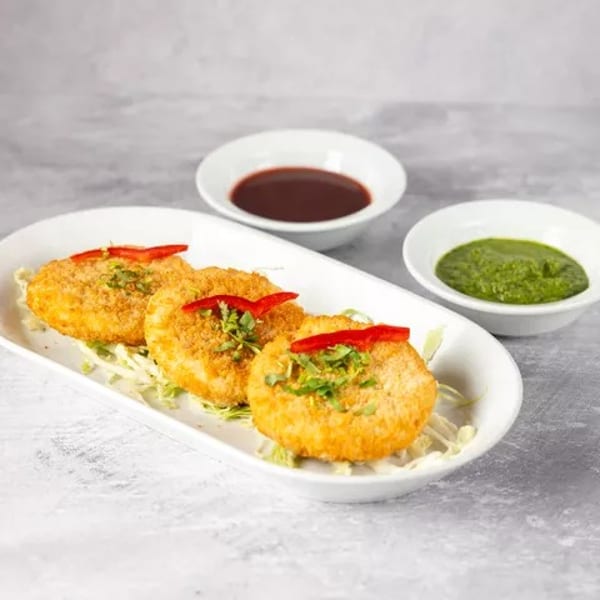 Three golden-brown fried patties garnished with herbs and red chili, served with two dipping sauces.