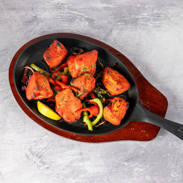 Sizzling chicken tikka with bell peppers and lemon on a cast iron skillet.