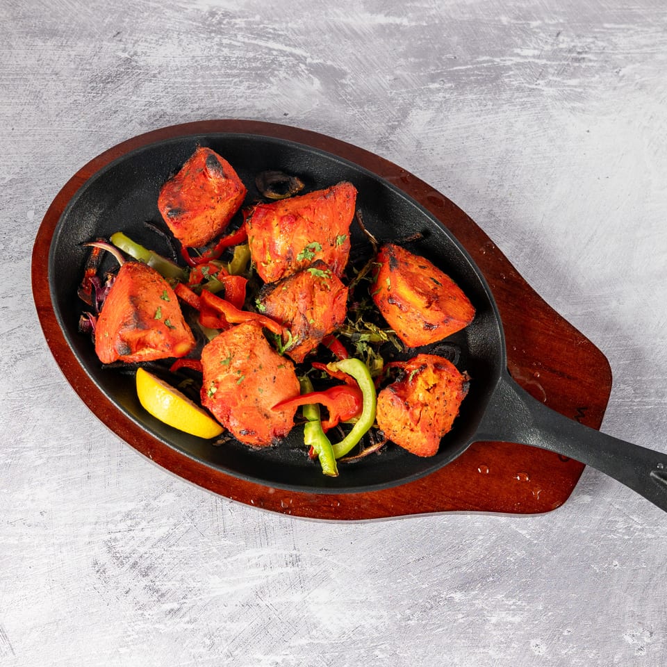 Sizzling chicken tikka with bell peppers and lemon on a cast iron skillet.
