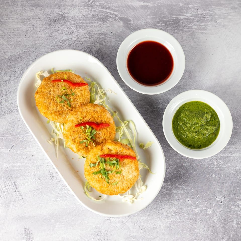 Three golden-brown fried patties on a white plate with shredded cabbage, served with two dipping sauces.