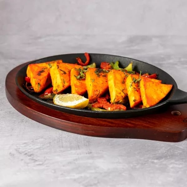 Sizzling paneer tikka with bell peppers and a lemon wedge in a black cast iron pan.