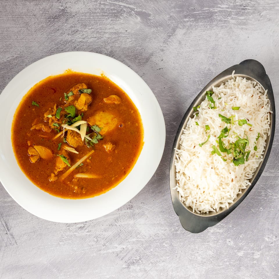 Chicken curry in a white bowl with a side of basmati rice in a metal dish.