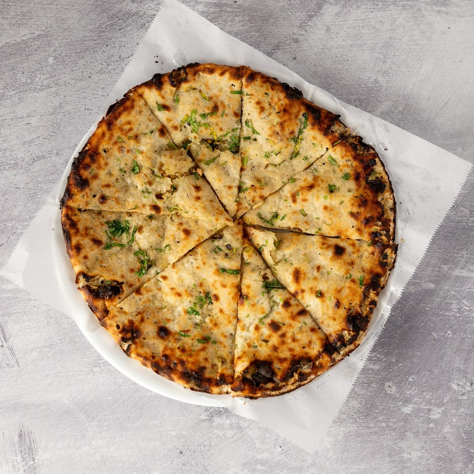 Round, sliced naan bread with green herbs and charred edges, served on white paper.