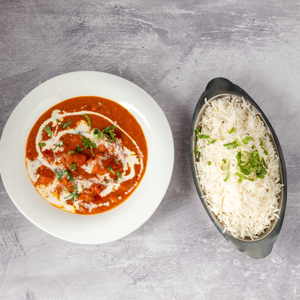 Chicken tikka masala with cream swirls and cilantro, served with a side of white rice.