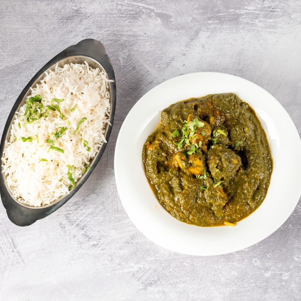 Top-down view of a white bowl of green chicken curry and a metal bowl of white rice.
