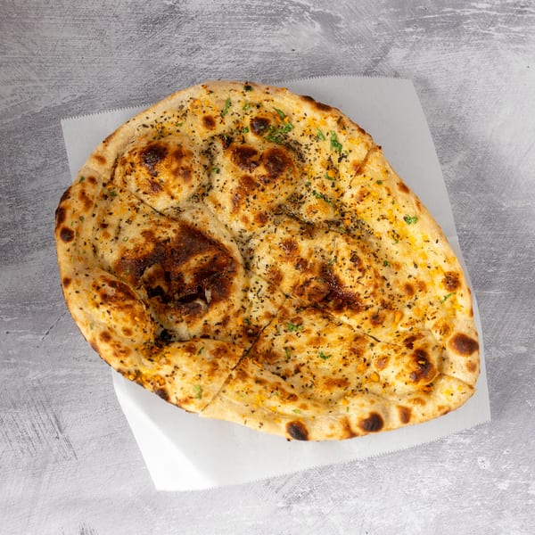 Golden-brown naan bread, garnished with herbs and spices, rests on white parchment paper.