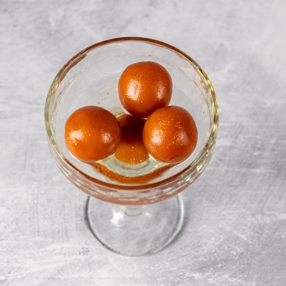 Three gulab jamun, Indian fried dough balls in syrup, in a clear glass dessert cup.
