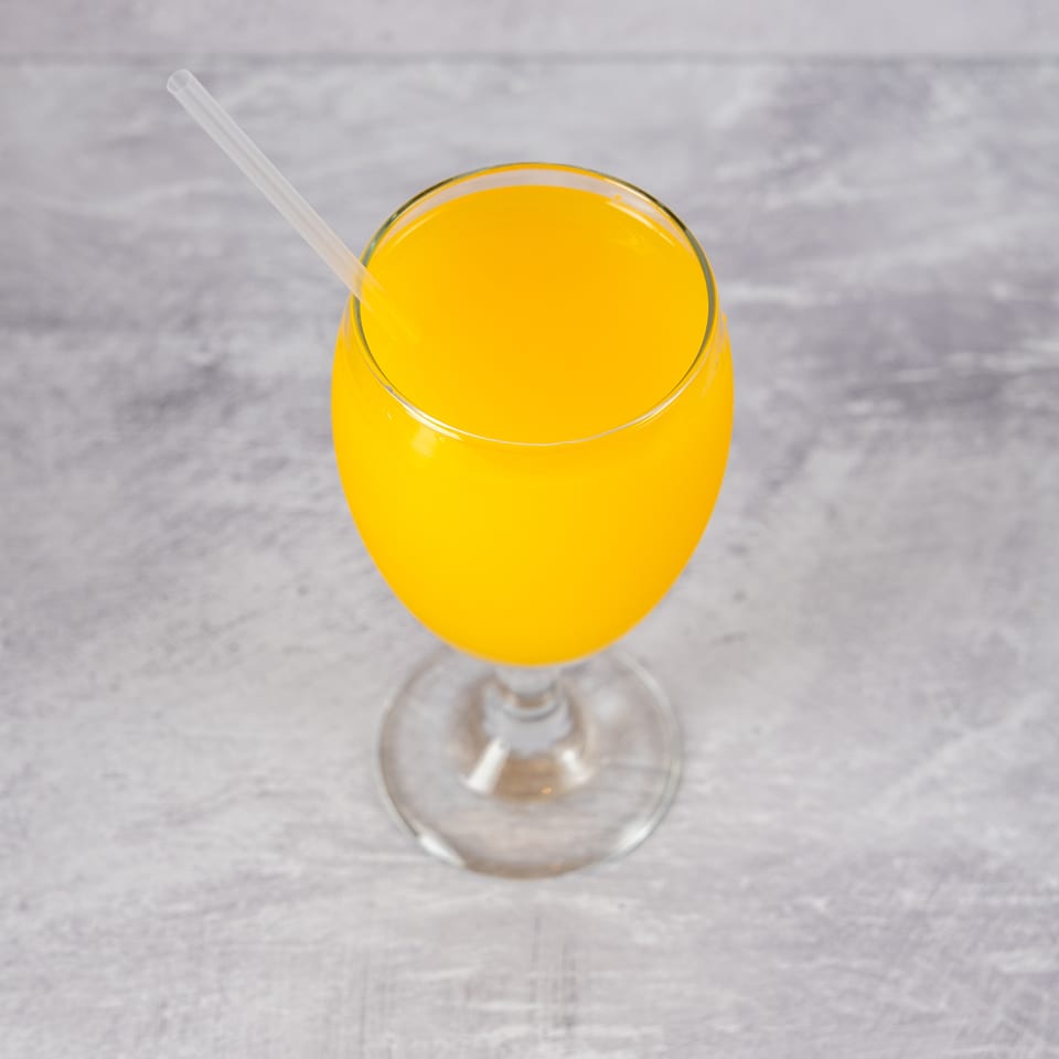A glass of bright orange juice with a clear straw, set against a light gray textured background.