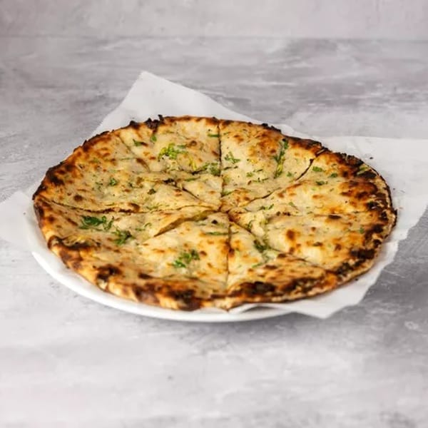 Round, sliced garlic naan bread with green herbs on a white plate and paper.